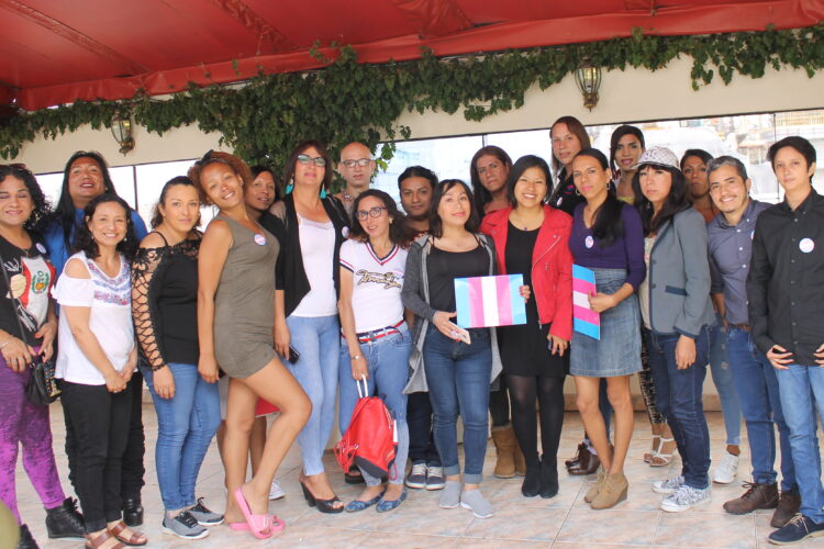 Group photo of trans activists in Peru holding the trans flag and standing outside under a red awning