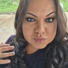 Yren Rotela selfie looking into the camera, wearing a black top with long brown hair and blue nailpolish.